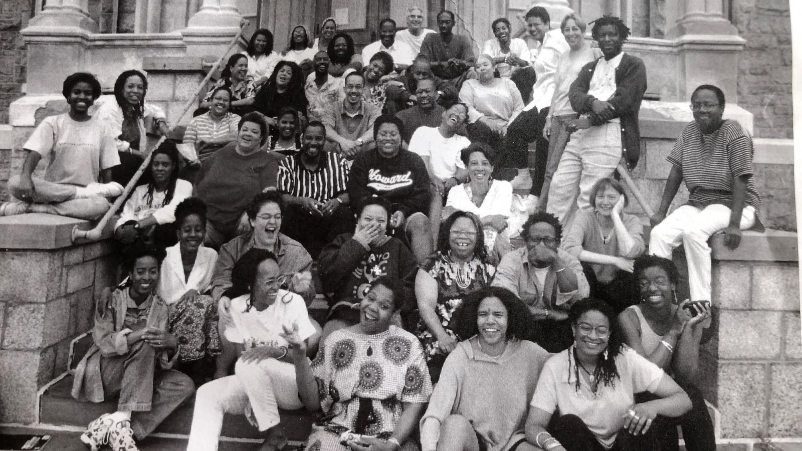 Black and white photo of a group of Black young people sitting on stairs in front of a building