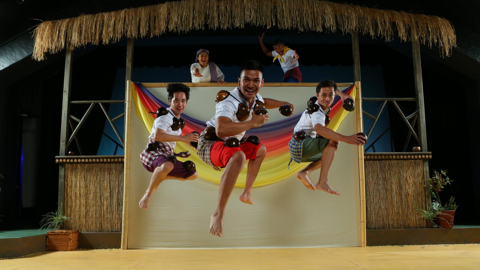 Three men onstage jump high in the air while actors behind them watch as they reenact a traditional Filipino folktale