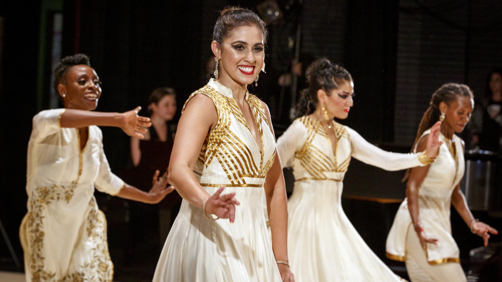 Four women dressed in white dancing on stage. 