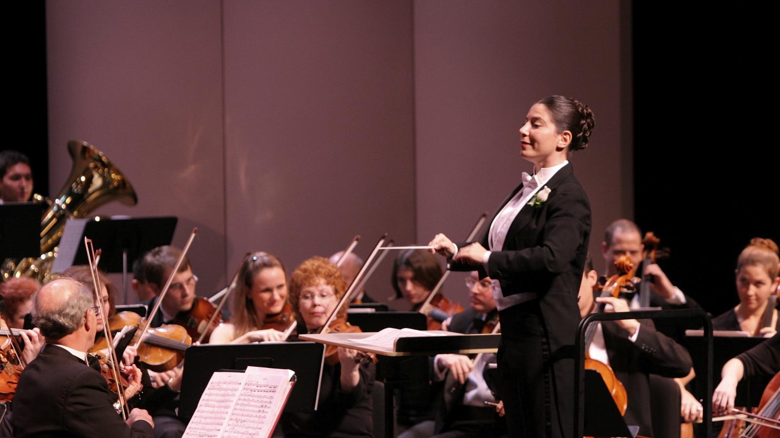Woman in tux leading an orchestra. 
