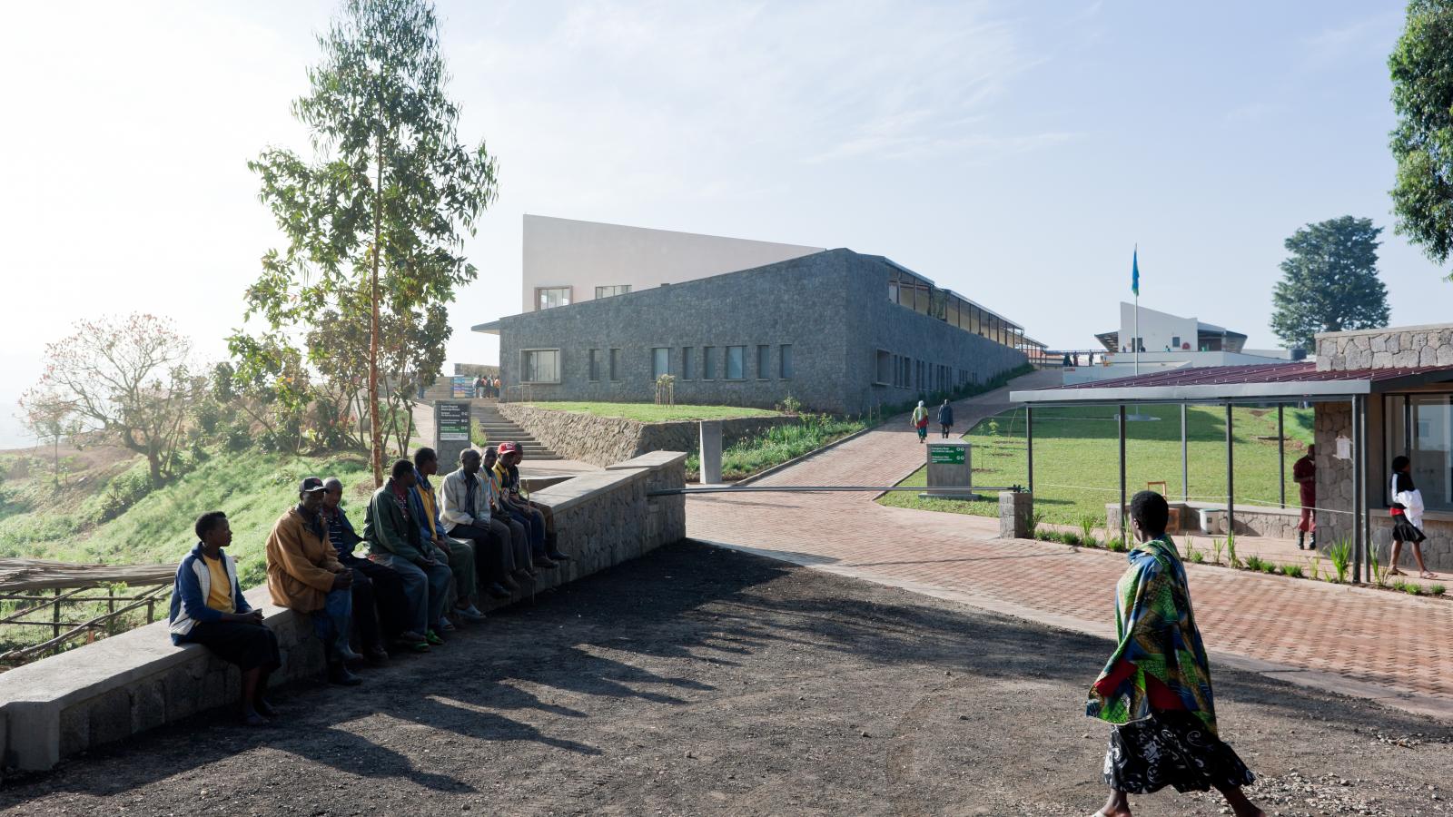 Butaro District Hospital People sit on a stone bench as another walk by outside of a hospital in Rwanda
