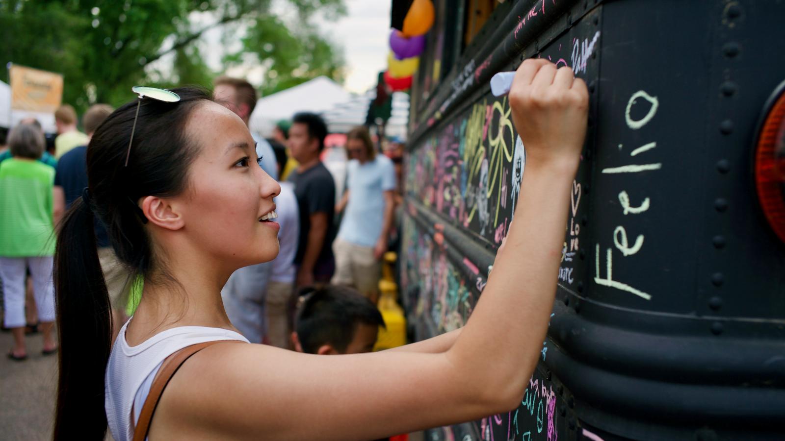 Young Asian woman with long hair in a ponytail writing on a wall. 