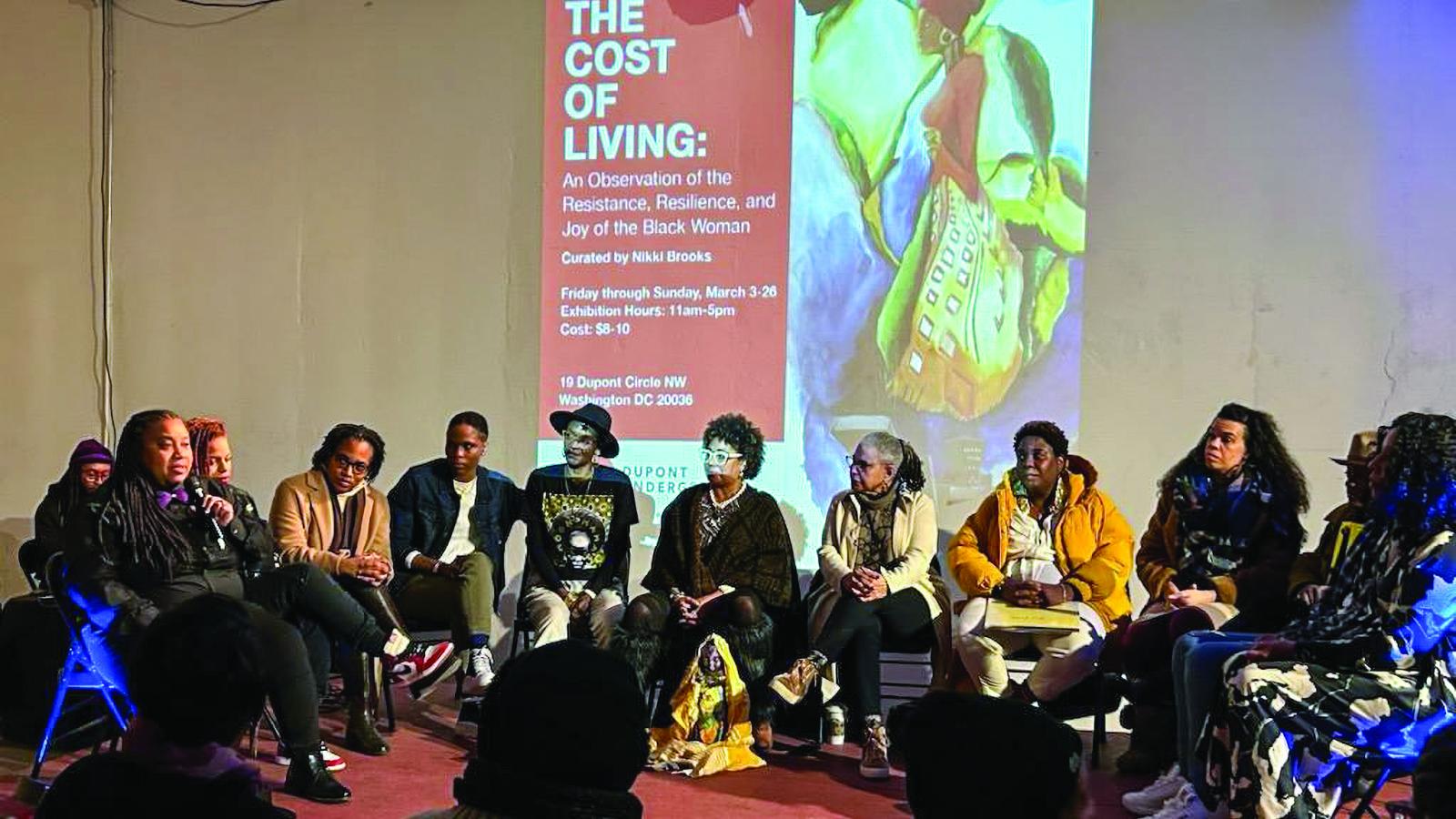 A group of Black women sitting in a circle on stage, one woman with a mic.