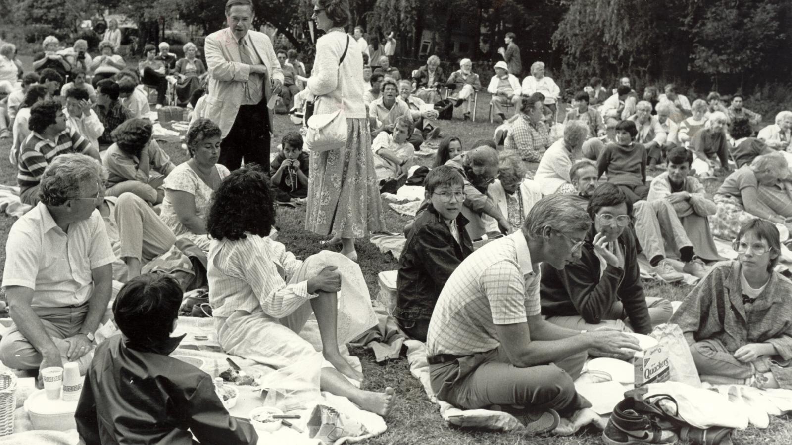 Crowd sitting on lawn for play. 