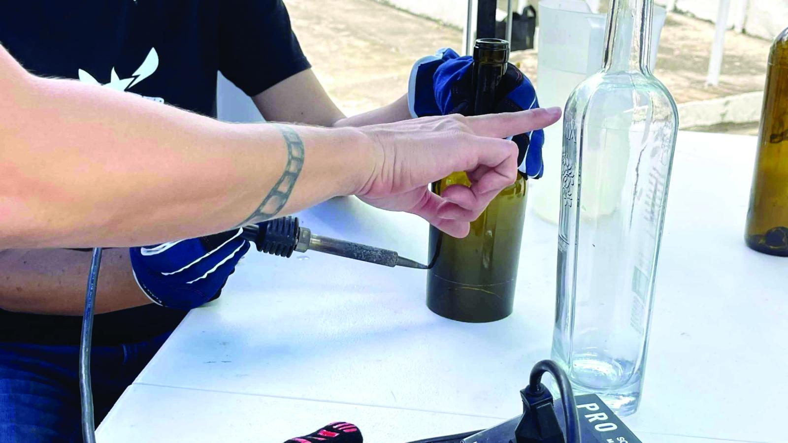 A hand pointing to a bottle on a table.