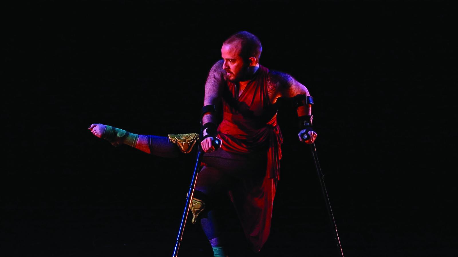 Man with short hair and beard on crutches dancing on stage.