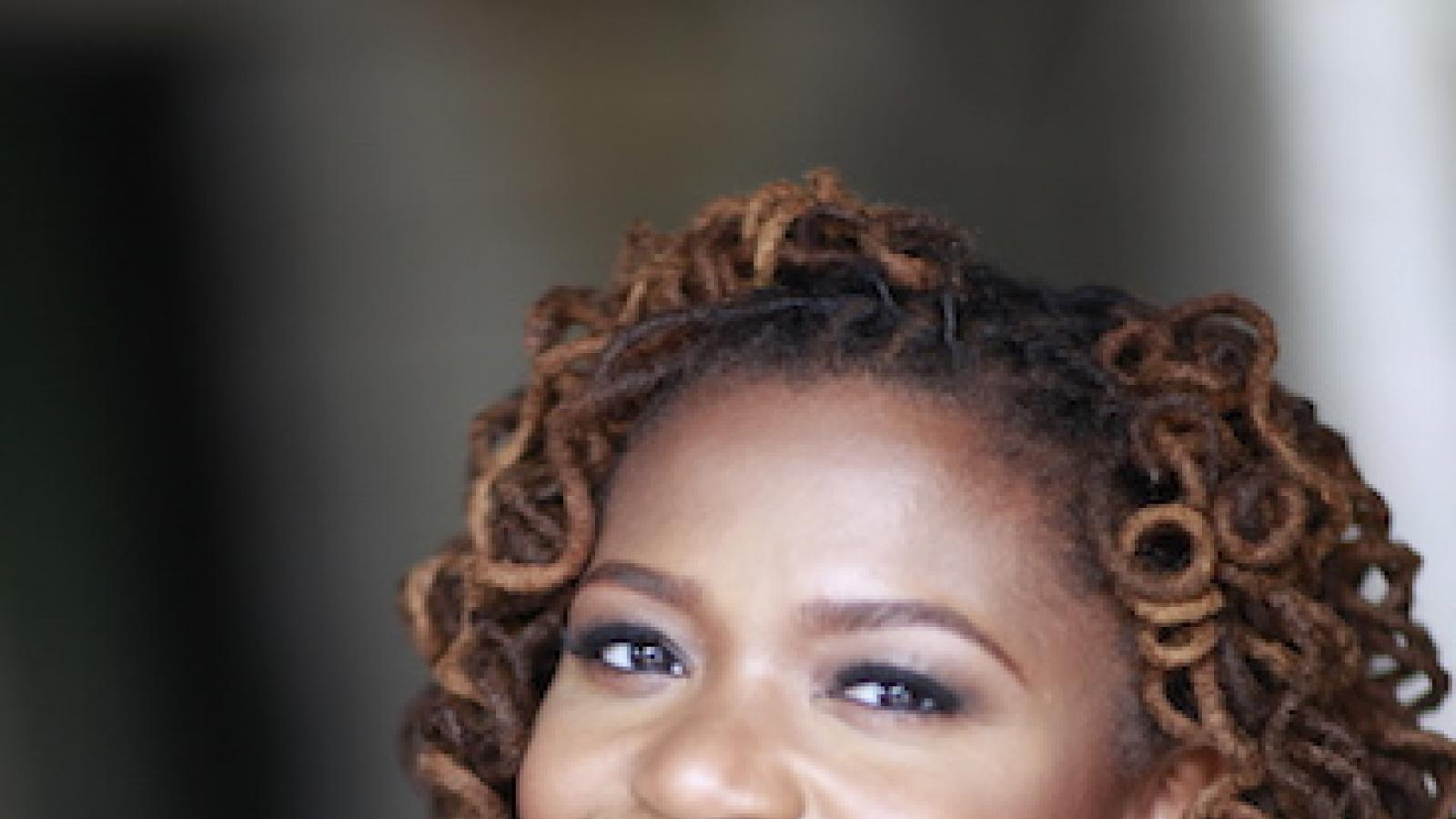 a smiling African-American woman with curly locs wearing a green blouse