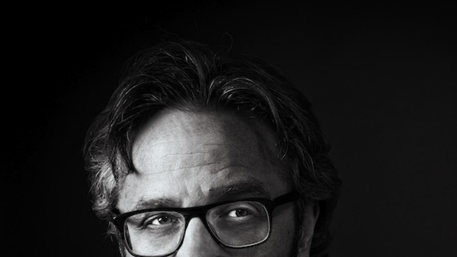 close-up of a white man with glasses and salt and pepper hair against a black background
