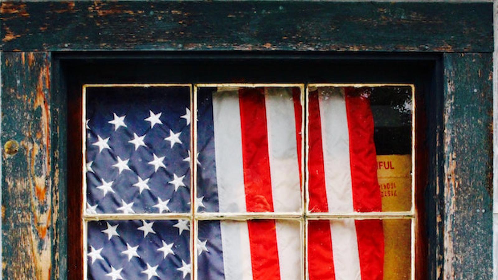 an American flag hangs curtain-like inside a blue wood-framed window