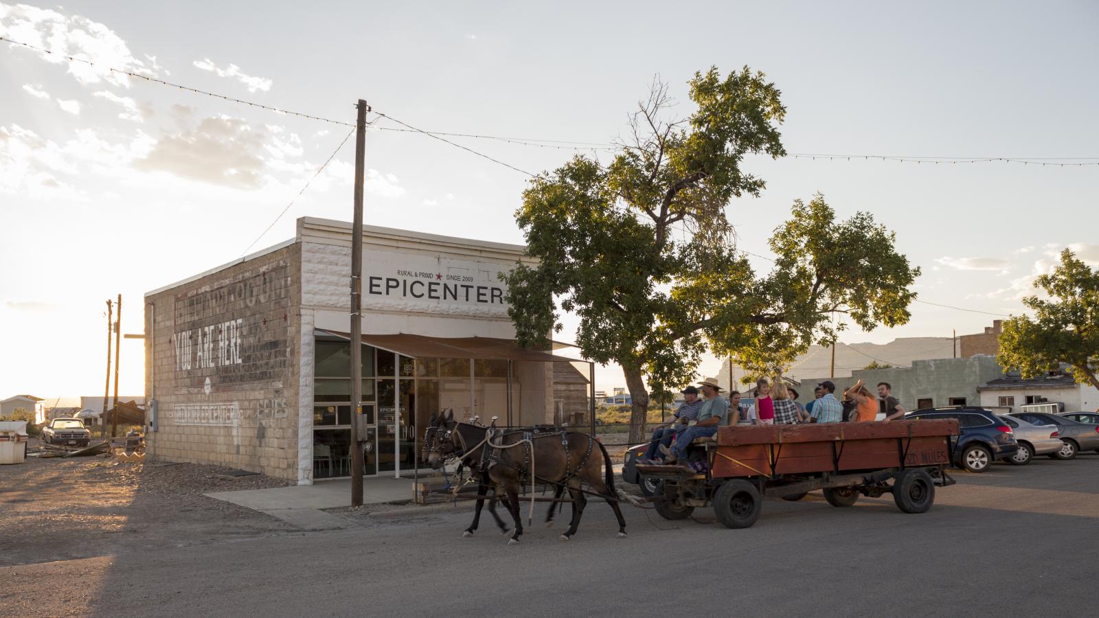 people in horse drawn cart in front of low building