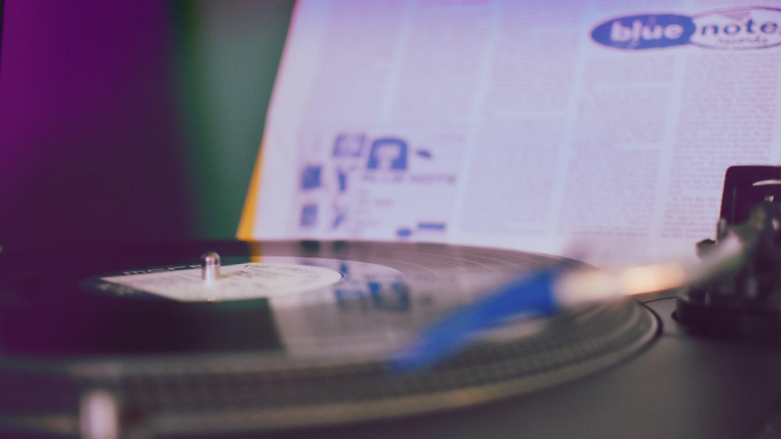 photograph of record player with record and back cover of a Blue Note album in the background