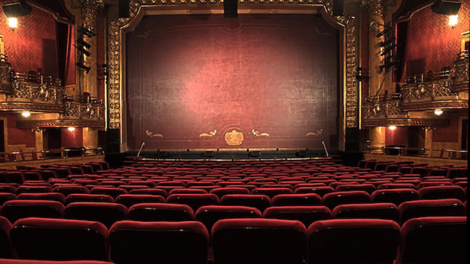 a theater auditorium with red velvet seats, boxes, a proscenium arch and a painted fire curtain