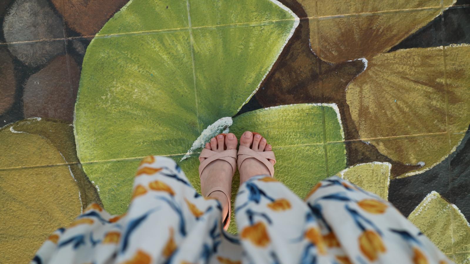 A woman in heels in a flower dress stepping over a sidewalk painting.