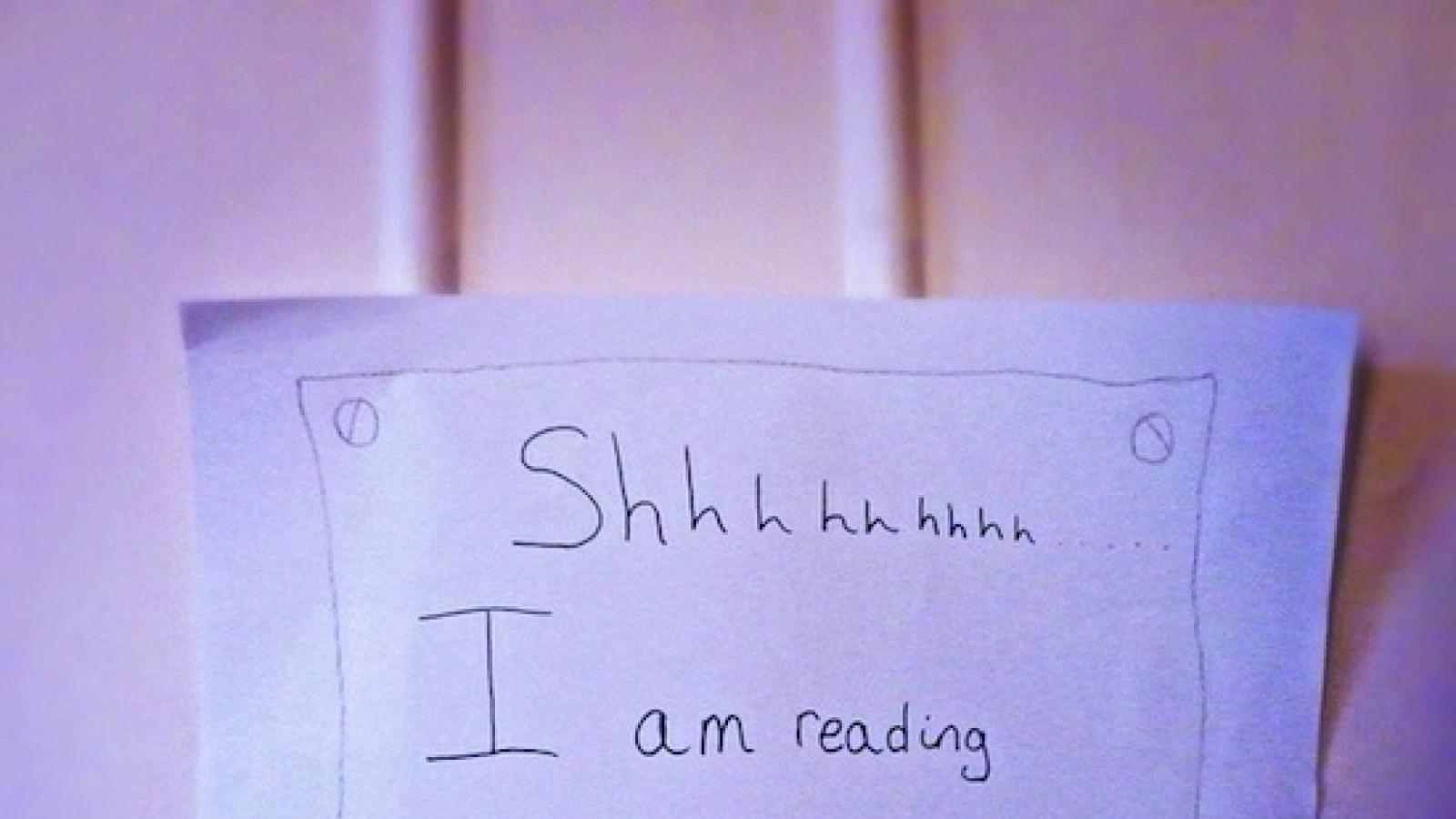 Close-up of a door with stickie note that says "Shhh, I am reading. Please knock. Thank you mum"