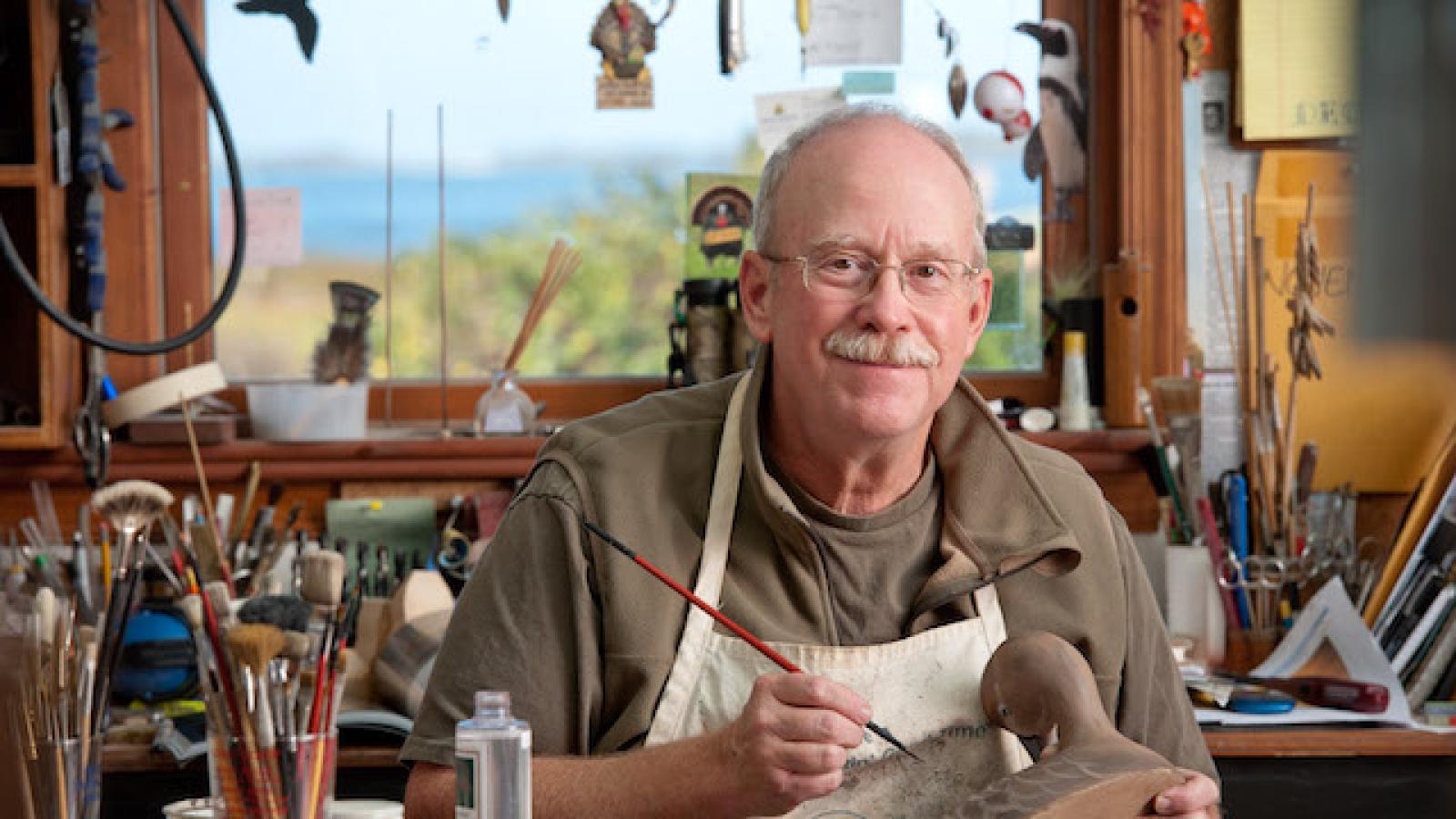 a man sitting in a workshop carving a duck decoy