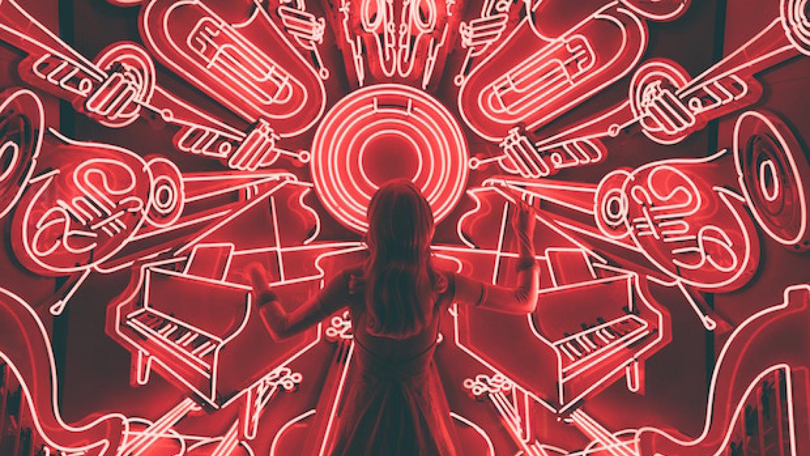 a girl stands in front of an image of a neon light drawing of several different types of musical instruments