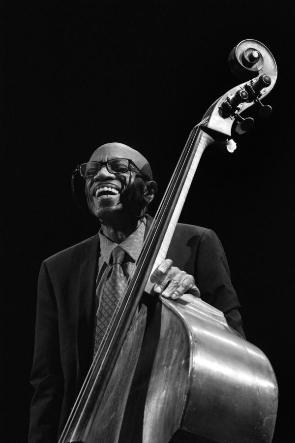 Man with glasses smiling holding an acoustic bass. 