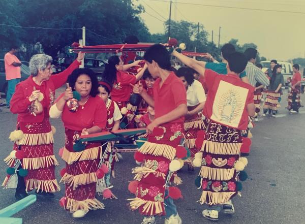 Group of women in colorful red outfits dancing in the street. 