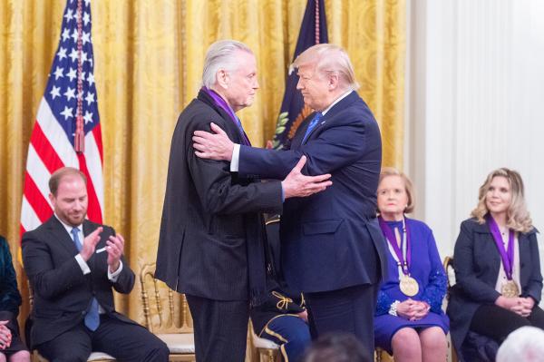 Two men in front of American flag embrace.