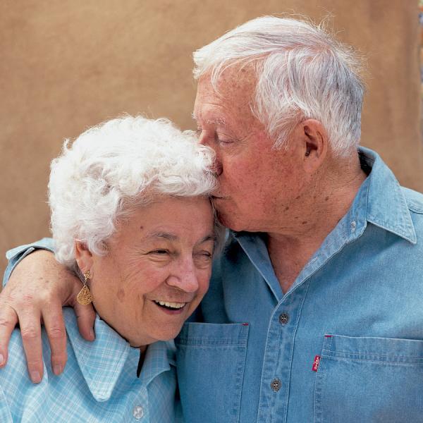 A man and a woman embrace. The man lands a kliss on the woman's head.