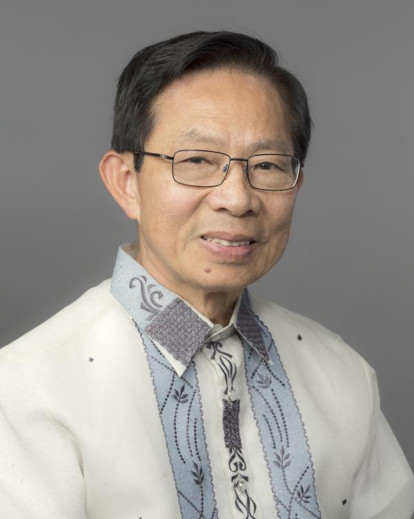 A man with dark brown hair and glasses wears a white, light blue, and grey collared shirt