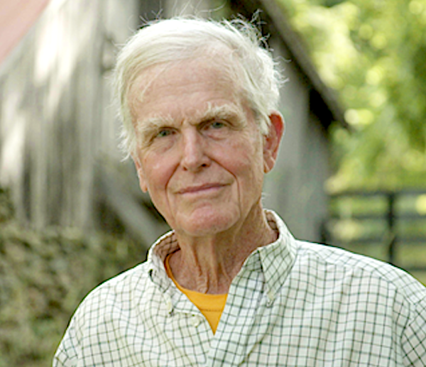 A man poses in front of a barn.