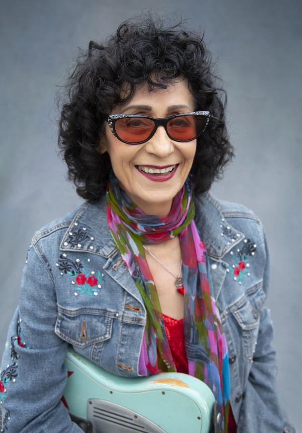 A woman in dark glasses holding a guitar.