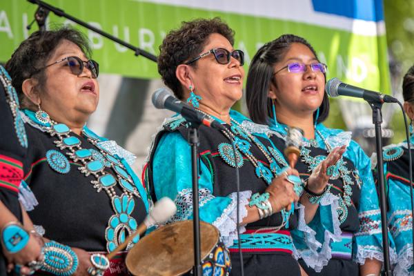 Three women singing from a stage.