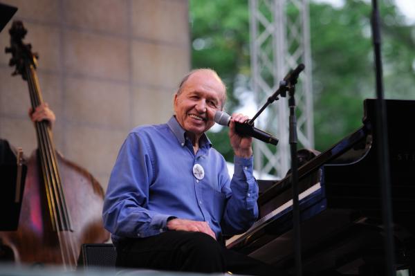 Man at piano on stage, smiling into camera.