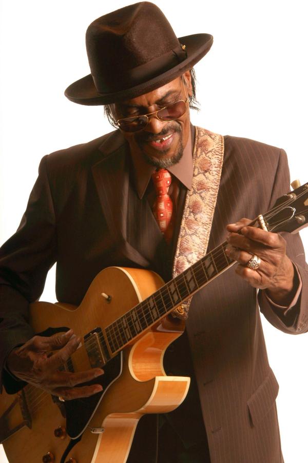 Man in hat and suit playing guitar.