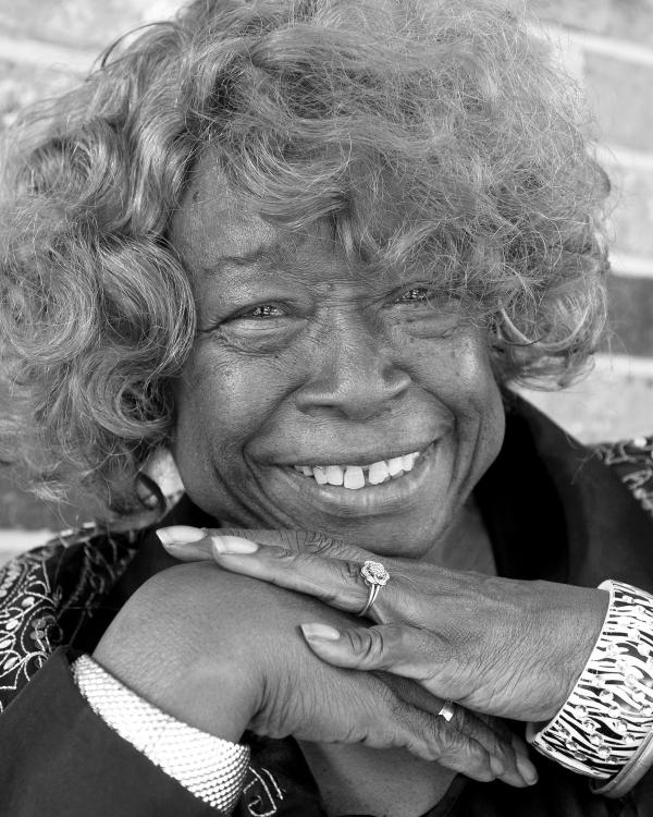 Portrait of Black woman with medium length curly hair smiling, her hands folded under her chin.. 