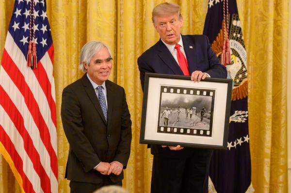 Man holding photo next to man by US flag.