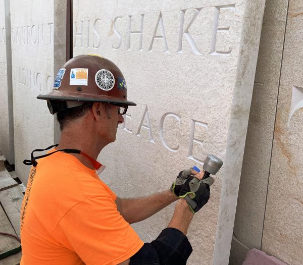 Man in hardhat and yellow shirt etching into stone. 