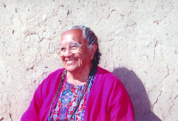 Older woman with gray hair and glasses wearing purple sweater against a white wall