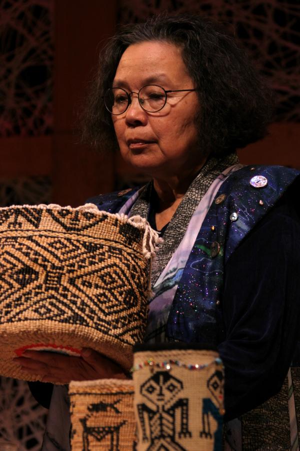 Native woman with glasses holding designed basket. 