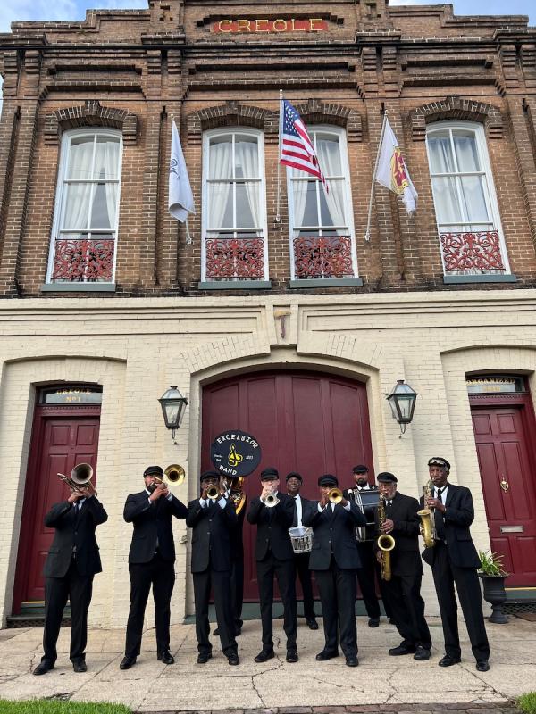 A band in uniforms plays in front of a two-story brick building.