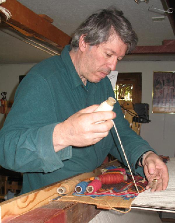 Man in blue shirt at a loom.