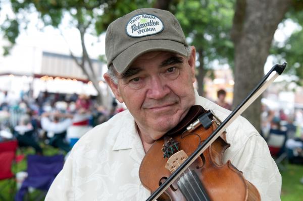 Man in baseball cap playing fiddle outdoors