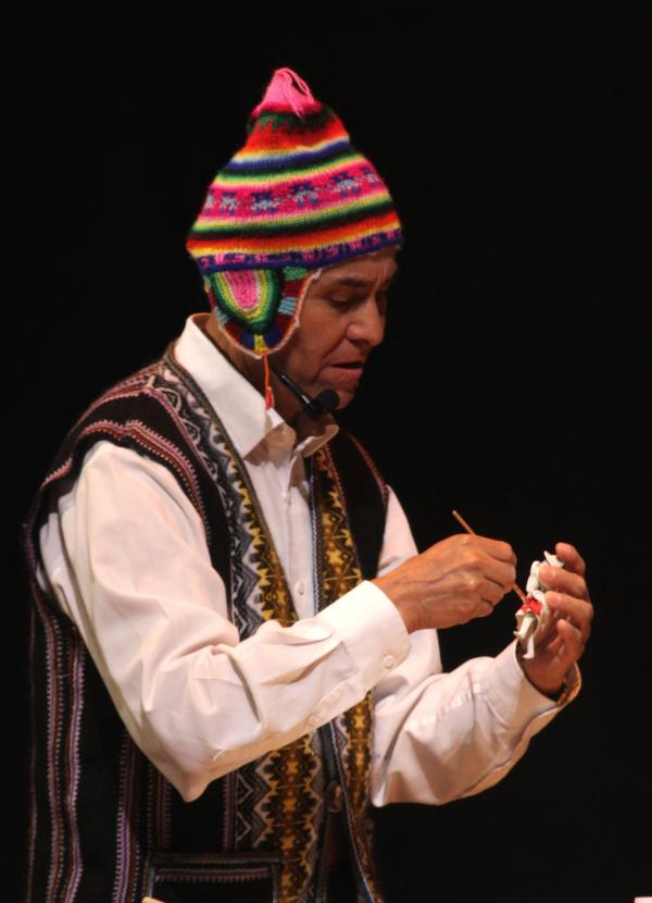 Man wearing a colorful Peruvian hat and vest painting an icon in his hand.