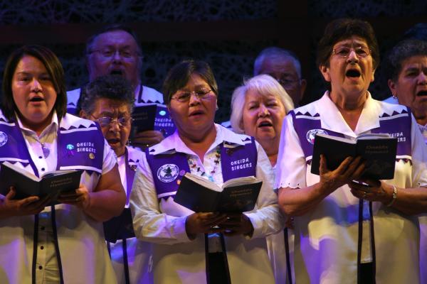 A group of women and men in robes holding hymn books singing. 