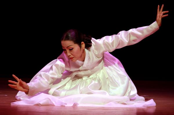 Asian woman with black hair tied back in a white dress in a dance position. 