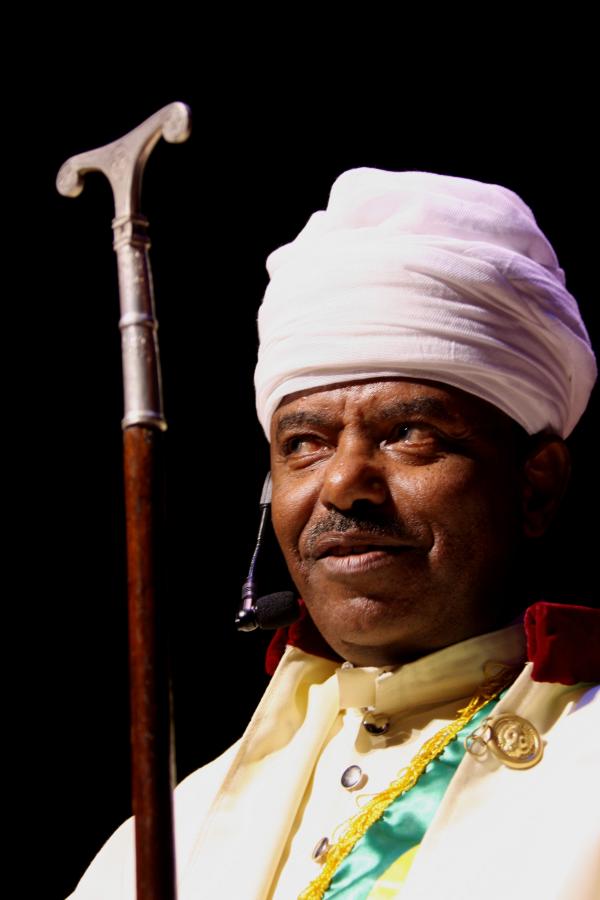 Black man wearing white turban and holding a cane with silver handle. 