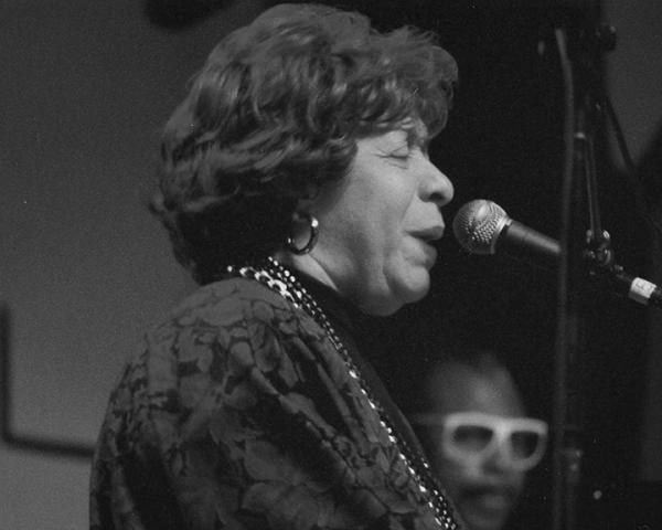 Woman at piano, singing.