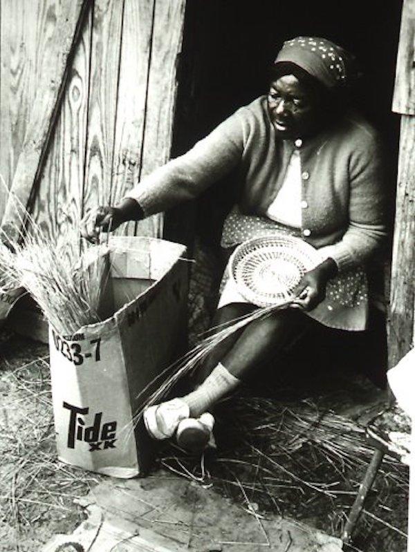 A woman making a wicker basket on her door step.