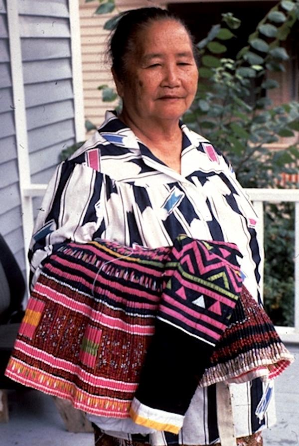 A woman holding weavings on her forearm.