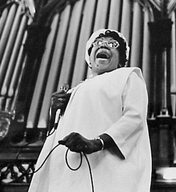 A woman singing in front of a large church organ.
