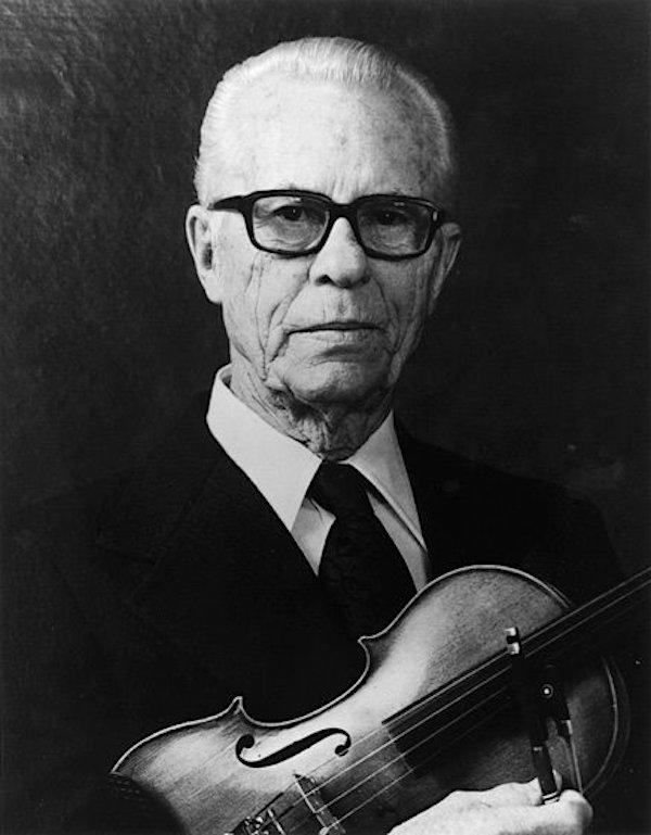 A man poses with a violin in his arms.