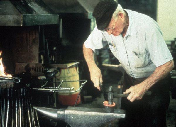 A man stooping over an anvil.