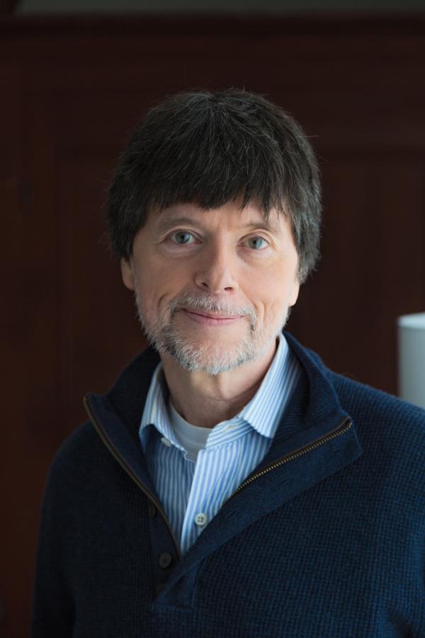 Man with short dark hair and gray beard wearing a sweater and dress shirt posing for portrait.