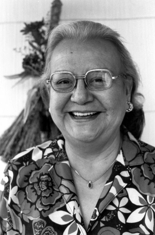Older woman with long gray hair wearing glasses, smiling. 